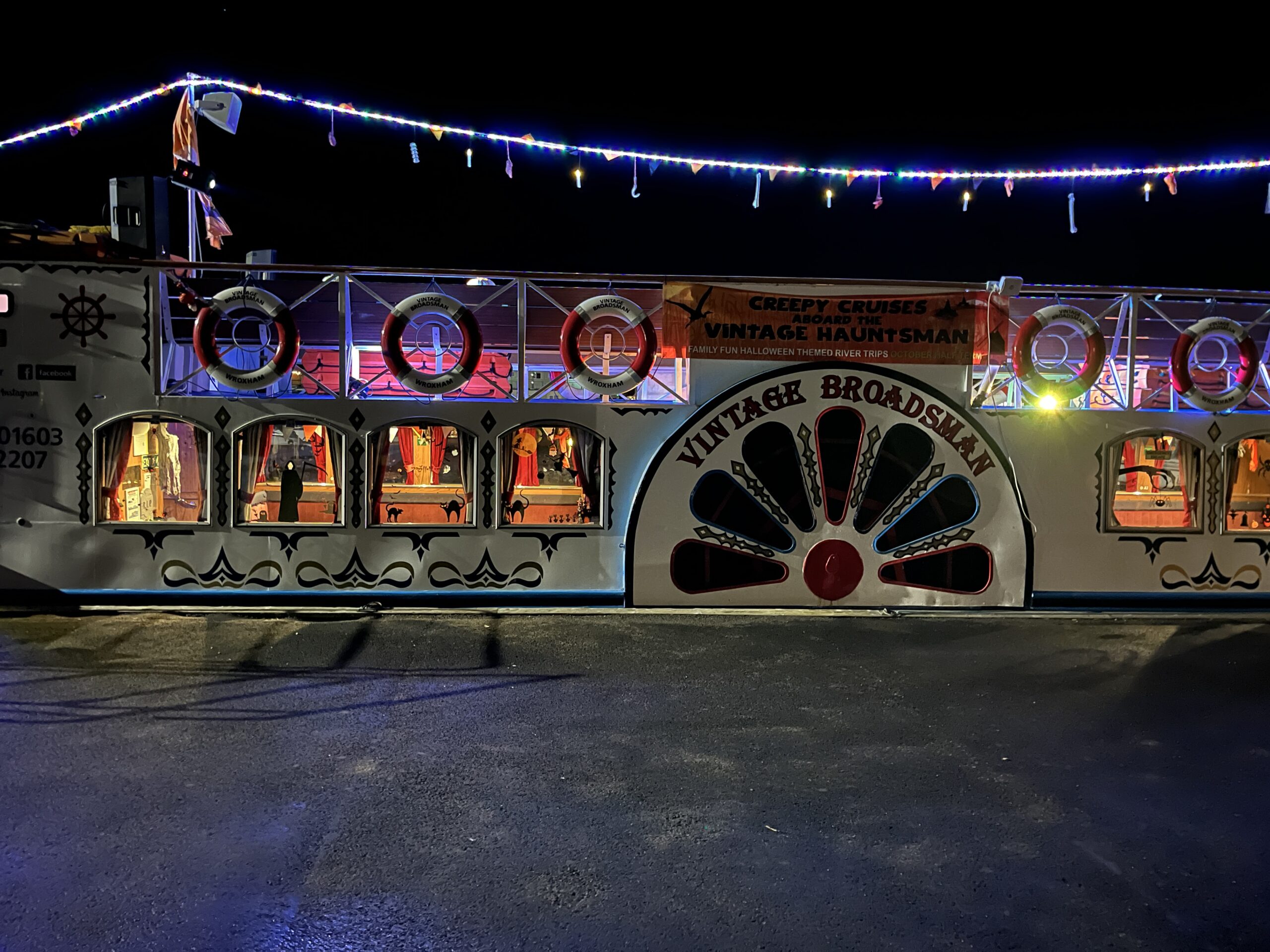 Vintage Broads cruiser decorated with spooky lights for a Halloween fancy dress party at night in Wroxham